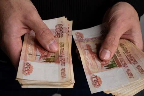 The hands of a man in close-up considers a bundle of Russian money to be five Stock Photos