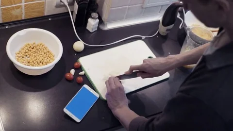 Hands of man cutting garlic at home kitchen and watching video at smartphone Stock Footage 74164352
