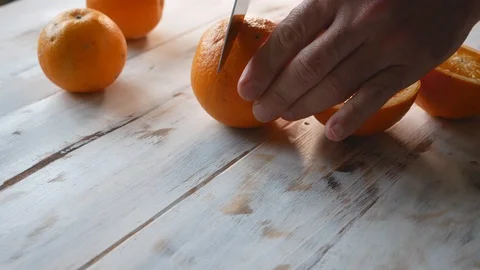 Hands of a man cutting oranges in halves on a wooden table Stock Footage 129394190