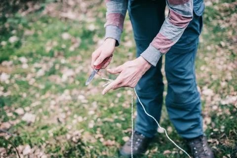 Hands of man cutting rope for preparing campsite. Stock Photos