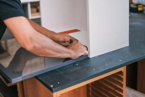 Hands of a man fixing a hinge on a surface for a kitchen. Stock Photos