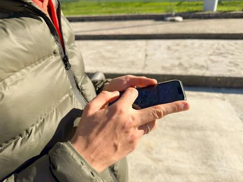 The hands of a man in a green jacket hold the phone close up Stock Photos