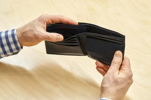 Hands of man hold empty black wallet against wooden table Stock Photos