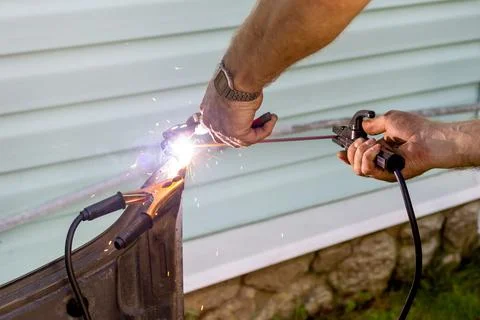The hands of a man hold a welding machine and are engaged in welding metal and Stock Photos