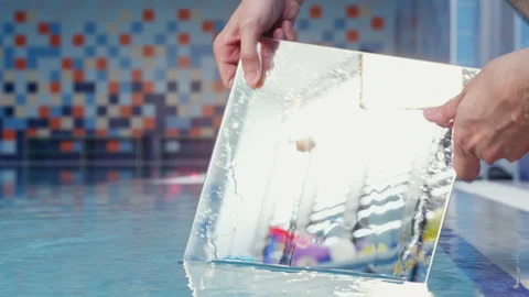 Hands of man immersing mirror into water of swimming pool Stock Footage 236708550