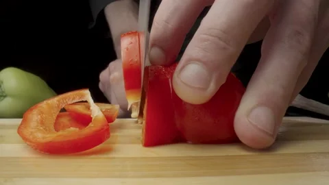 Hands of man with knife cutting red sweet pepper on black background. Process of Stock Footage 203025332
