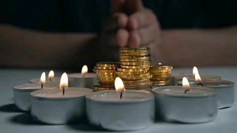 Hands of man praying circle made of burning candles with a stack of coins inside Stock Footage 129469373