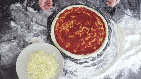 Hands of man sprinkle cheese on dough for pizza with tomato paste top view Stock Footage 127694729