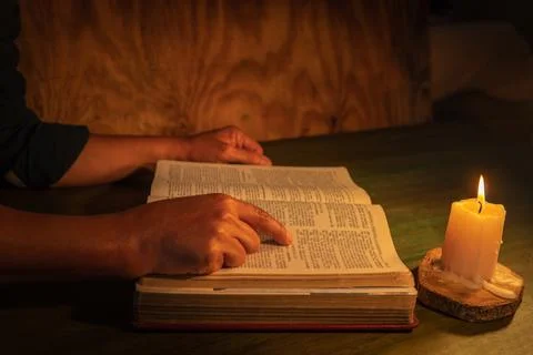 Hands of a man studying the bible pointing to a biblical passage by candlelig Stock Photos