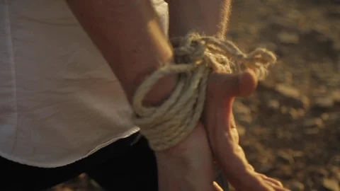 Hands of man tied in the back by a thick rope struggling in the Moroccan desert Video stock 110768108