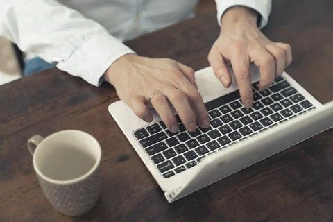 Hands of a man working on laptop placed on rustic wooden table with an empty cup Stock Photos