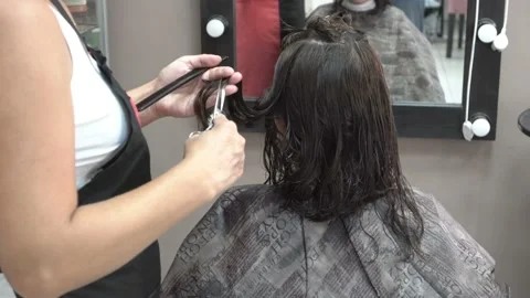 The hands of a master barber close-up. He cuts the dark hair of a girl  Видео 111897054