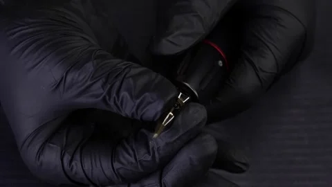 Hands of the master with black gloves are holding a tattoo machine and trying Stock Footage 165541070