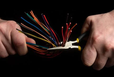 Hands of the master hold diagonal pliers and wire closeup on black background Stock Photos