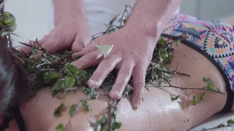 Hands of master put branches and massages back of girl lying on couch in spa Stock Footage 154243596