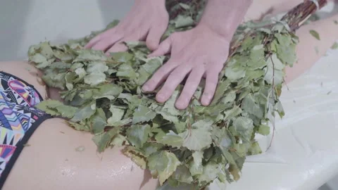 Hands of master put broom and massages legs of girl lying on couch in spa salon Stock Footage 154243770