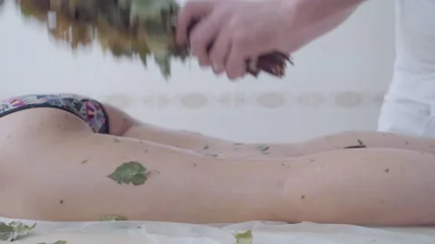 Hands of master put broom and massages body of girl lying on couch in spa salon Stock Footage 154243789