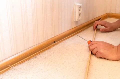 Hands measuring and aligning baseboard molding in carpeted room Stock Photos