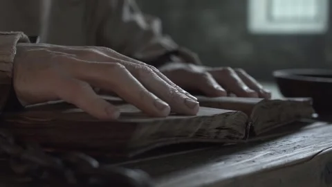 Hands of a medieval prisoner in chains tracing lines on pages of a book 스톡 동영상 339231311
