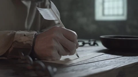 Hands of medieval prisoner in shackles writing with a quill pen on table Stock Footage 339231468