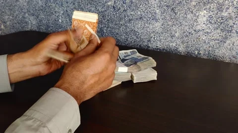 Hands meticulously count Pakistani rupee notes on a brown wooden table Stock Footage 303688618