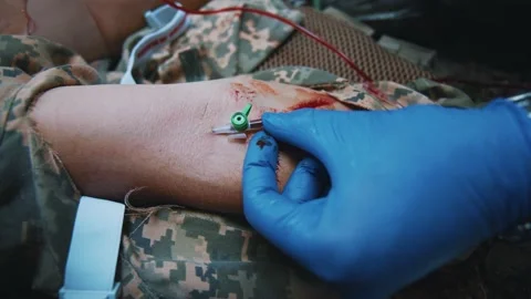 Hands military medic provides first aid to a soldier who inserts a needle into a Stock Footage