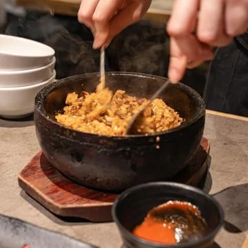 Hands mixing cooked rice inside a hot stone bowl with visible steam. The ac.. Foto stock