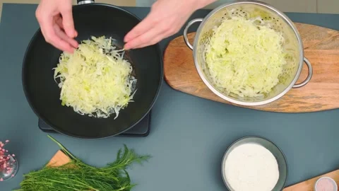 Hands mixing shredded cabbage in a metal bowl on kitchen cutting board Stock Footage 342889151