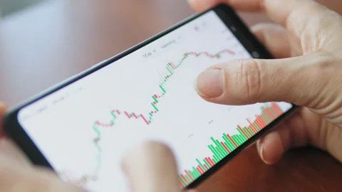 Hands with a mobile phone, checking stock market data. Scrolling through Stock Footage 218450680