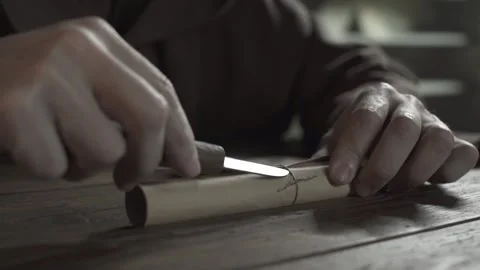 Hands of a monastic scribe with a penknife cutting string on a scroll 스톡 동영상 337930081