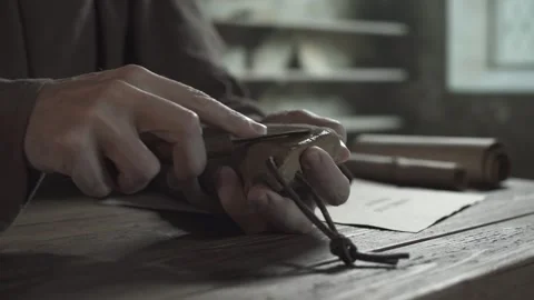 Hands of a monastic scribe sharpening a penknife blade on a wet grindstone Video stock 337930180