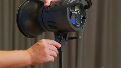 Hands mounting studio flash on light stand close-up, securing strobe unit into Stock Footage 333650139