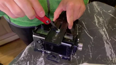 Hands mounting tripod plate on camera cage close-up, tightening screw to secure 動画素材 333649585