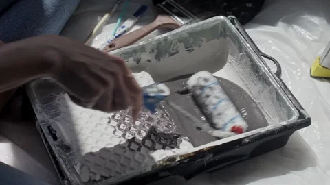 Hands move paint roller through paint tray on protected floor. Stock Footage 334813940