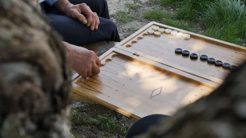 The hands of an old and young man playing backgammon on a park bench throwing Video stock 194812474