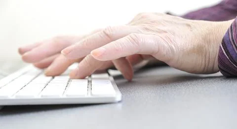 Hands of an old female typing on the keyboard, isolated on white, close-up. Stock Photos