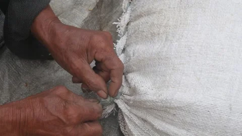 The hands of an old man untying the rope of a sack containing rice Stock Footage 316923332