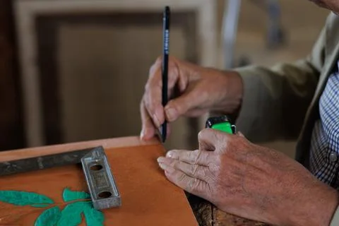 Hands of an older man, working on embossed leather, and taking notes. Stock Photos