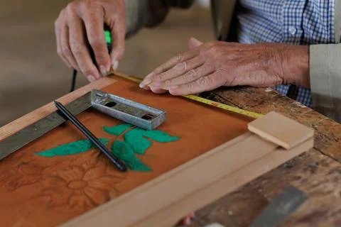 Hands of an older man, working on embossed leather, and taking notes. Stock Photos