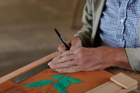Hands of an older man, working on embossed leather, and taking notes. Stock Photos