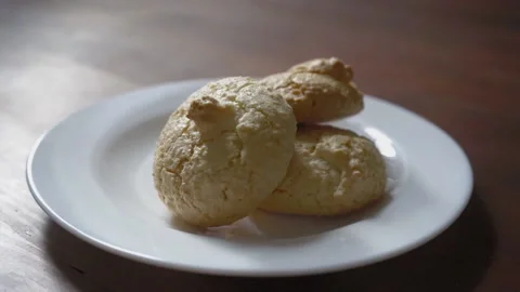 Hands one by one take cookie off the white plate standing on the dark wooden Stock Footage 133629401