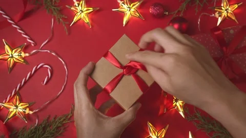 Hands open gift box with bow on the red background of Christmas New Year deco Video stock 220951360