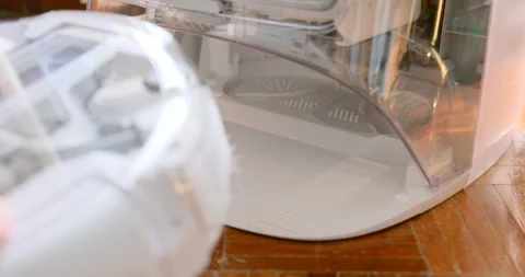 Hands open a robot vacuum self-emptying dock and check the base on a wooden Stock Footage 327843238
