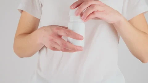 Hands opened a vial of pills over white background studio wall. No inscriptions. Stock Footage 279070016