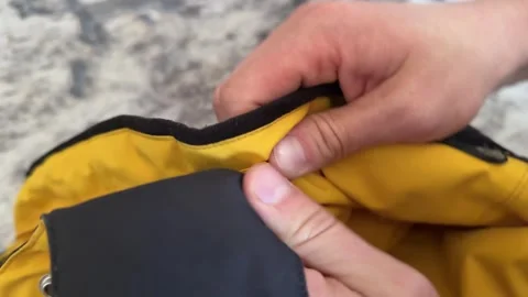 Hands opening and closing a metal snap button on the hood of a yellow jacket. Stock Footage 336976590