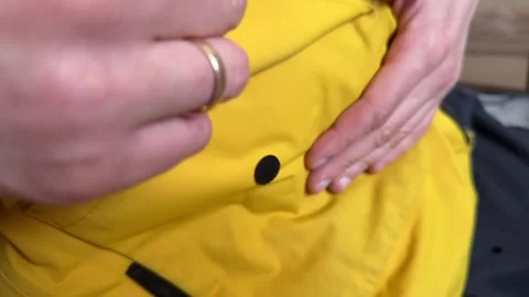 Hands opening and closing a snap button pocket on a yellow jacket. Close up of Stock Footage 336976585