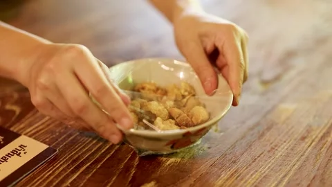 Hands Opening a Bowl of Crispy Pork Cracklings on Wooden Table 스톡 동영상 338377736