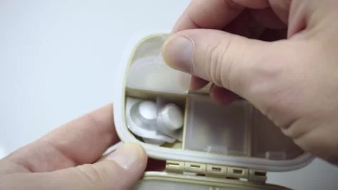 Hands opening pill organizer with tablets inside close up medication storage Stock Footage 342512708