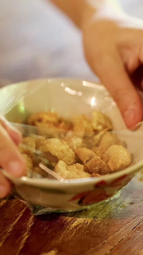 Hands Opening Plastic Wrap on Bowl of Crispy Pork Cracklings Stock Footage 339870934