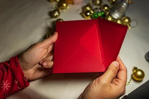 Hands opening red Christmas envelope with holiday decor Stock Photos